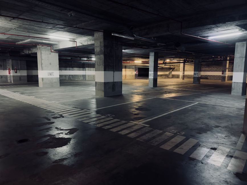 A moody underground parking garage featuring empty spaces and puddles on the floor.